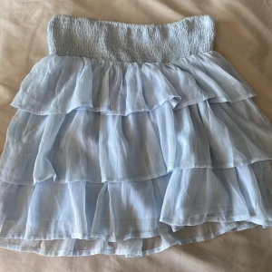 Kjol - Ljusblå kjol med volanger i lager. Använd max 5 gånger. Inga skador.