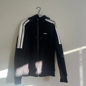 Hugo Boss kofta - Svart Hugo Boss kofta med vita och gråa detaljer. Knappt använd. Storlek S. Nypris 1399kr