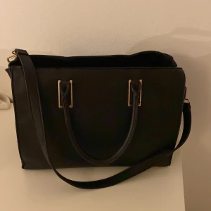 Stor svart väska - Stor svart väska med guldiga detaljer, mycket utrymme.