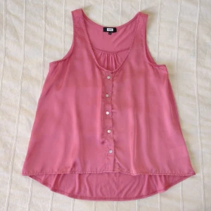 Rosa v-ringad lös topp/linne i glansigt tyg, storlek S - Linne från Bik Bok med v-ringning och knäppning i fram. Så fin mörkare gammelrosa färg. Tyget på framsidan är sidonliknande med fin lyster/glans. Bakdelen är längre och i vanligt matt tyg. Använt någon enstaka gång. 80% polyester 20% viskos. Storlek S.