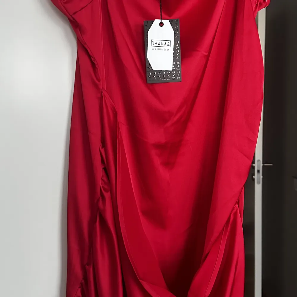 Röd kort klänning, helt ny oanvänd. Omlottdesign. Glansigt tyg, med rynk framtill. Oanvänd  Nypris 609. Klänningar.