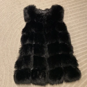 Svart pälsväst från Veraldo  - Svart väst i fuskpäls. Knäpps med hyska och hake. Sidfickor. Satinfoder. Fint skick.