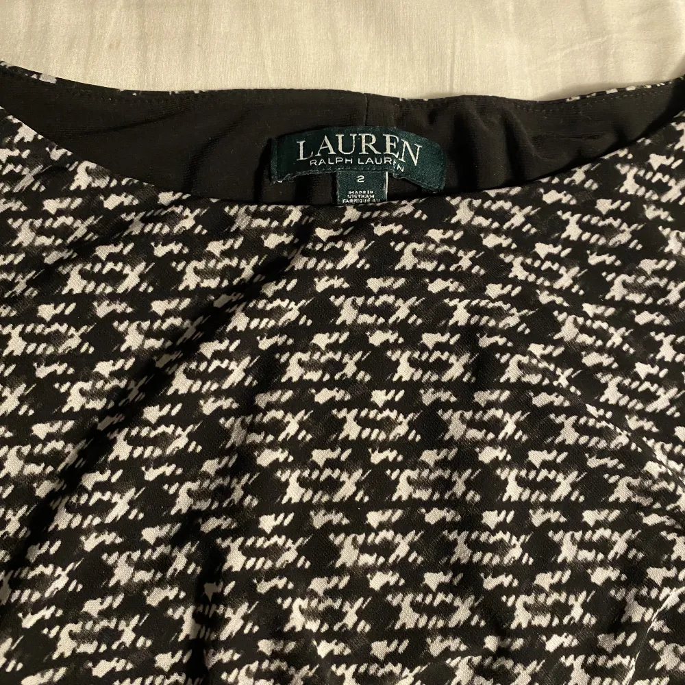 Klänning från Ralph Lauren i ett svartvitt mönster. Finns en kort slits på vänstra sidan. Relativt tjockt tyg så kan användas även vintertid. Två svarta ränder går på vardera sida av klänningen.. Klänningar.