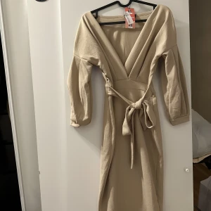 Beige långklänning - Helt oanvänd beige långklänning som har ett band runt midjan och är yringad väldigt fin och bra i materialet i storlek S
