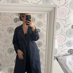 Marinblå trenchcoat  - Säljer denna fina trenchcoaten från bershka i storlek xs. Endast använd 2 gånger och är i fint skick! Den kommer ej till användning längre tyvärr! 