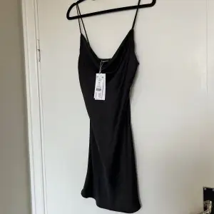 Den perfekta svarta lilla klänningen ifrån Gina Tricot i storlek 38. Klänningen har en vattenfallsurringning med justerbara smala axelband. Aldrig använd och har prislapp kvar. 