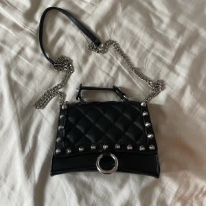 Svart väska med detaljer - En jättefin väska som knappt är använd och som är i nyskick, den har silvriga detaljer och kedjan är avtagbar så man kan ha den som både en handväska och en väska som man kan ha över kroppen! Vid snabb affär kan priset diskuteras 