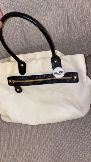 Moschino väska - Säljer min Moschino väska, väskan har använts några gånger och har synliga bruna fläckar inuti väskan, pga smink. Därav priset :) 