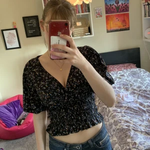 Blommig svart topp med puffärm - Blommig topp med puffärm. Nyskick. Köpt från BikBok. Längst när är materialet ”reflat” och stretchigt. Tryck gärna på köp nu :)