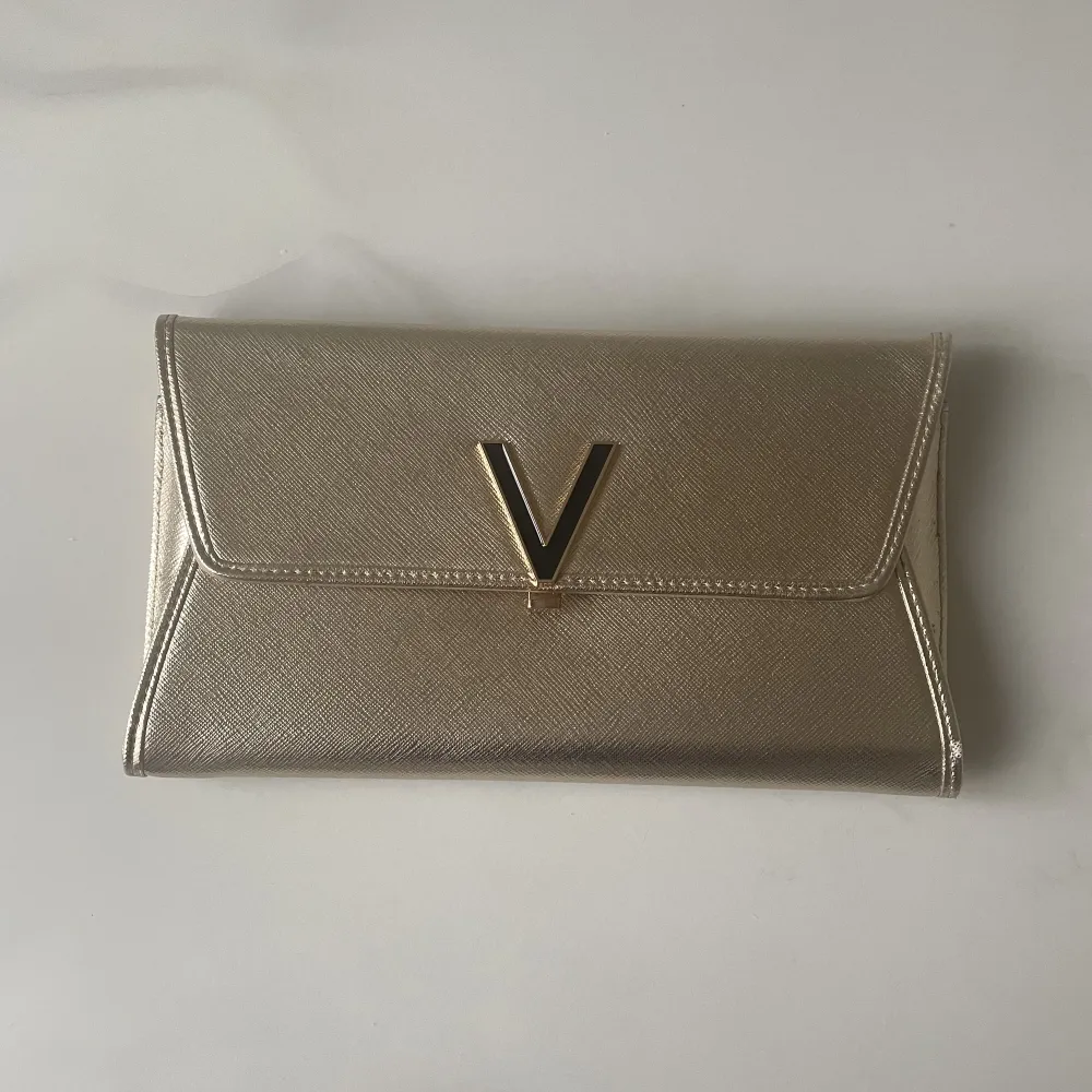 Väska från Valentino by MarioValentino i guld/champagnefärg. Kan bäras som kuvertväska eller på axeln/crossover med medföljande kedja. Väskan är endast använd en - två gånger så är som ny.. Väskor.