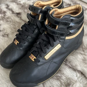 Helt oanvända Reebok Hi Tops i svart och guld - Helt oanvända Reebok Hi Tops i svart och guld. Storlek 36