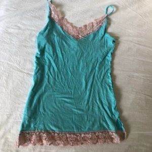 Y2K spetslinne strl S - Ett turkost linne med rosa spetsdetlajer, i gott skick, från gamla Gina Tricot.  Byst: 33cm  Midja: 32cm Höft: 37cm  Längd från armhåla: 40 cm.  Köparen står för frakt. Dma gärna vid frågor eller funderingar:)