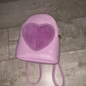 Väska - Jättegullig väska med ett hjärta på som är fluffig! Väskan är lite mindre i storleken vilket gör den enkel att ha med sig💕Använd men inga synliga defekter:) Skriv ifall ni har ngr frågor🩷