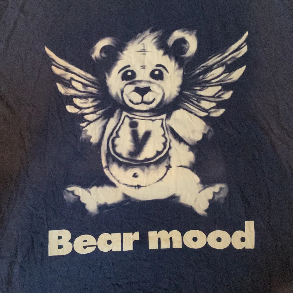 Marinblå t-shirt med en nallebjörn på med ängel vingar. Bra skick förutom ett litet hål vid ryggen som knappt är synligt. Material: 100% bomull. T-shirts.