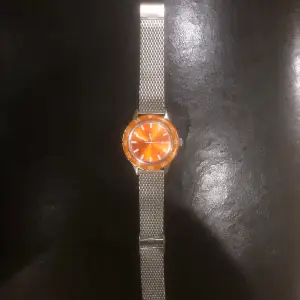 En orange gant klocka som man kan justera storleken på. Lite repig på glaset, utöver det är den en solklar klocka.