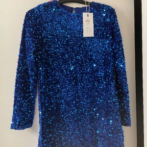 Blå glittrig klänning - En fin nyårsklänning. Aldrig andvänd, prislapp kvar. Storlek S, Ganska kort i modellen men annars normal passform. 