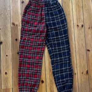 Punk-byxor - Rutiga byckor i tyg. En sida är rödrutig och en sida är grön och svart. Det finns hål för bälten och skärp. Jag brukar också hänga kedjor och accessoarer i de öglorna. Tyget är som ett kraftigare pyjamastyg. Skriv vid frågor!