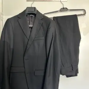 En fin svart kostym från Riley som använts en gång. Paketet inkluderar en svart kostym dvs byxor och blazer samt en svart skjorta. Storleken på byxorna är 44, kavajen är 46 och skjortan är i xs. Jag var ca 167 cm när den satt perfekt.