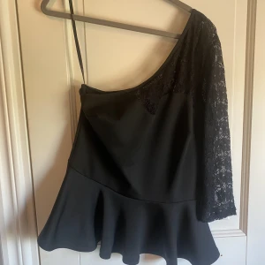 Svart festtopp - Svart topp med en trekvartsärm i spets och utsvängd nedtill. Toppen är använd vid ett tillfälle och köpt på Primark. Storlek 40.