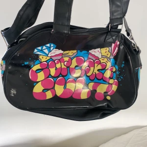 Mellanstor väska - cupcake cult - En SUPER snygg mellanstor väska med graffiti tryck med ett stort ytterfack och ett i mitten med fack innuti, tre band både ett längre som går att ta av och justera längden på samt två kortare!!💗😇