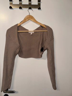 Kort cardigan - En kortare cardigan med långa armar, stickad material i beige färg, den har sytts upp ytters långt upp men inget som påverkar plagget. 