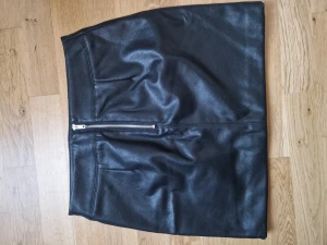 Kjol i skinnimitation - Svart kjol i skinnimitation m. Storlek 40. Använd en gång så den är i nyskick. Dragkedja bak.