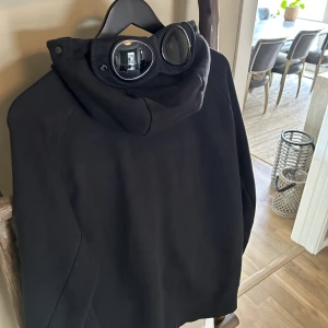 C.P Company  - Svart hoodie med glasögon på luvan som man kan fälla ner Bra skick inga hål eller märken nästan som ny  Köpt på care of carl  Storlek L passar även M