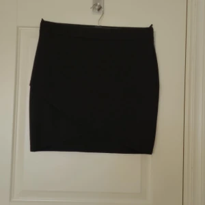 Svart kjol - Kort svar kjol med skimmer. Vacker detalj på framsidan. Aldrig använd. 