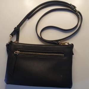 En cirka 21×13 cm liten svart väska med borttagbara band. En liten fläck på framsidan men syns knappt. Inte använd mycket och i bra skick.