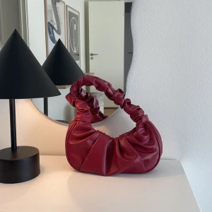 Röd Liten Väska - Vinröd/Burgundy färgad liten söt väska. Säljer då den aldirg kommer till användning. Sömmen har gått upp lite i innertyget. 
