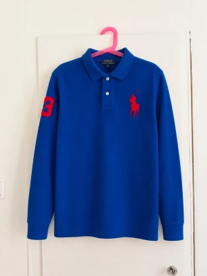 Polo Ralph Lauren långärmad piké i snygg klarblå färg med röda detaljer 🔵🔴 - Klassisk Big Pony-modell med stor broderad röd Polo-logga på bröstet och nummer 3 på ärmen. Väldigt snygg färgkombination och perfekt till höst/vår eller som lager under en jacka. • Storlek M (10–12) • Polo Ralph Lauren • Big Pony-logga • Långärmad • Klarblå med röda detaljer • Klassisk pikékrage • Fint skick men lite missfärgad i kragen! Skriv gärna vid frågor eller om du vill ha mått!