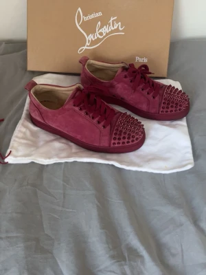 Vinröda Christian Louboutin skor - Säljer ett par vinröda sneakers från Christian Louboutin i mocka- storlek 40, sjävklart äkta. Originalförpackning, extra skosnören medkommer.