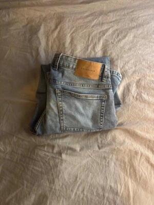 Ljusblå raka jeans från Smog (baggy) - Säljer ett par ljusblå jeans från Smog med klassisk femficksmodell och raka ben. Jeansen har en snygg tvättad look och detaljer som läderpatch bak i midjan. Perfekta för en avslappnad och trendig stil. (Strlk 31/30)