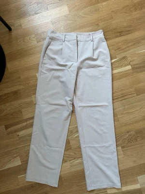 Raka kostymbyxor - Snygga beige kostymbyxor med raka ben och pressveck. Byxorna har hällor för skärp och sidofickor.  Använda fåtal gånger.
