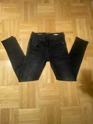 Svarta Replay Anbass Hyperflex - Säljer ett par svarta skinny jeans med lätt slitna detaljer och klassisk femficksmodell. Jeansen har smal passform och bälteshällor i midjan. Materialet är stretchigt och bekvämt, perfekt för en trendig vardagslook.