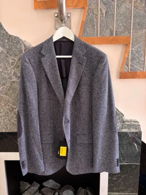 HUGO BOSS kavaj – helt ny med tags – strl 50 - Säljer en helt oanvänd HUGO BOSS-kavaj i mörkblå/navy, storlek 50. Mycket snygg, stilren modell med diskret struktur i tyget och klassisk passform.  Helt ny och oanvänd – alla tags sitter kvar • Modell: Jestor2 • Färg: Navy • Storlek: 50 • Två knappar framtill • Bröstficka och fickor framtill • Snygga detaljer på armbågarna • Perfekt både till fest, jobb och mer dressad vardag