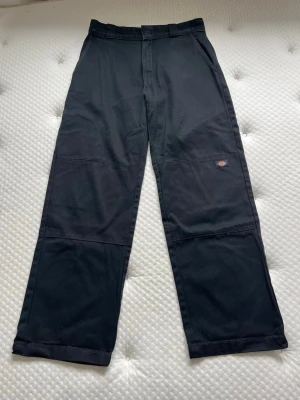 Loose fit baggy dickies svarta byxor jeans - Svarta jeans från dickies i modellen loose fit, dvs baggy. Har dubbla tyg över knäna (bild 2). Och knäpps med en ”hake” istället för knapp (bild 4). Jeansen är i helhet i superfint skick men är noppriga på insidan (bild 6) dock inte noppriga på utsidan. De har dessvärre även använts uppvikta och har till följd av detta fått hål längst ner på benen (bild 7). Går att kapa nedtill eller använda uppvikta så syns inte hålen.   Midjemått: 40cm Innerbenslängd: 79,5cm Grenhöjd: 27,5cm Benvidd (mätt läng