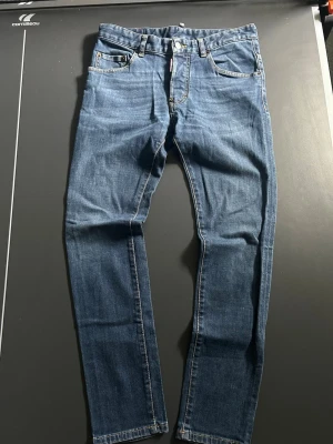 Blå slim fit jeans från Dsquared2 - Säljer ett par blå slim fit jeans från Dsquared2 med klassisk femficksmodell och snygga kontrastsömmar. Jeansen har en skinnpatch med logga bak i midjan och är tillverkade i mjukt denimtyg. Perfekta för en trendig och avslappnad look.