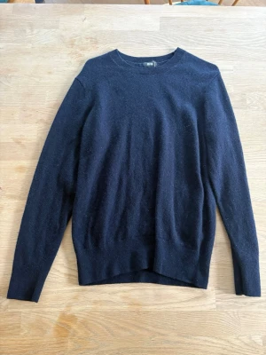 Cashmere tröja - En klassisk svart stickad tröja med rund hals och långa ärmar. Tröjan har en enkel och stilren design, perfekt för lager på lager. Materialet ser ut att vara en mjuk ullmix som håller dig varm under kyliga dagar.