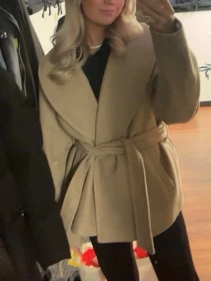Beige kappa från Vero Moda - Säljer en beige kappa från Vero Moda i storlek L. Jackan har en oversized passform med bred krage och dragkedja framtill. Materialet är mjukt och känns som ullblandning, perfekt för höst och vinter. Snygg och enkel att styla med dina favoritjeans.
