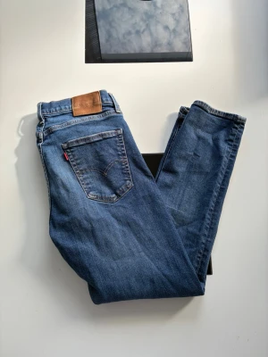 Blå raka jeans från Levi's - Klassiska blå jeans från Levi's med rak passform och fem fickor. Jeansen har en snygg tvättad look, silverfärgade nitar och den ikoniska läderpatchen bak i midjan. Tillverkade i slitstark denim med en cool vintagekänsla.