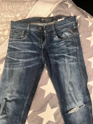 Fc barcelona replay 32/34 limitited anbass - Säljer ett par blå jeans från Replay med snygga slitningar och en trasig detalj vid knät. Klassisk femficksmodell med dragkedja och knapp. Jeansen har en tvättad look och kontrastsömmar. Perfekta för dig som gillar en avslappnad och trendig stil.