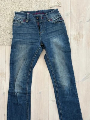 Bondelid jeans - Snygga mörkblå jeans med raka ben och diskreta slitningar på framsidan. Insydda i midjan. Jeansen har kontrastsömmar och detaljer i rosa vid fickorna. Perfekta för en avslappnad och trendig look.