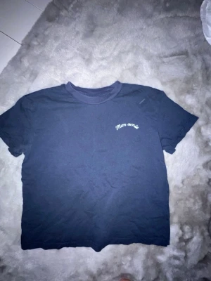 Mörkblå t-shirt med texttryck - Snygg mörkblå t-shirt med vit text 'Mon amie' på bröstet och större tryck på ryggen. Klassisk rund hals och korta ärmar. Perfekt för en avslappnad och trendig look.