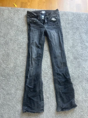 Grå bootcut jeans från Gina Tricot - Snygga grå bootcut jeans från Gina Tricot med slitningar och två knappar i midjan. Jeansen har klassisk femficksdesign och är tillverkade i denim med lite stretch för skön passform. Perfekta för en trendig och avslappnad look.