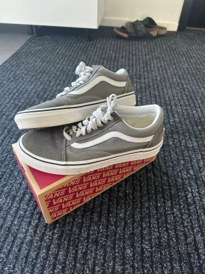 Gråa Vans Old Skool sneakers - Gråa Vans Old Skool sneakers med vit sula och klassisk vit sidostripe. Skorna har vita skosnören och ovandel i mocka och canvas. Perfekta för en avslappnad streetwear-look och passar till det mesta i garderoben. I mycket gott skick utan defekter. 