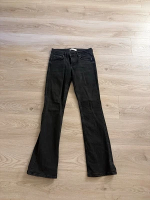 Svarta bootcut jeans - Säljer ett par svarta bootcut jeans med klassisk femficksdesign och normal midja. Jeansen har utsvängda ben och är tillverkade i ett mjukt denimtyg som ger en snygg siluett. Perfekta för dig som gillar en retroinspirerad look.