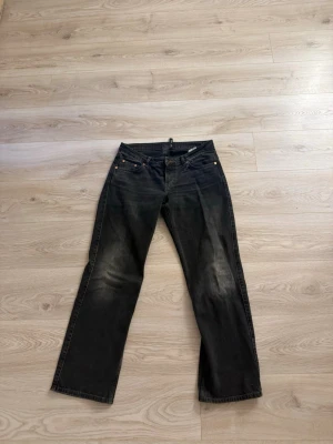Svarta raka jeans med slitningar - Ett par svarta jeans med raka ben och lätt slitna detaljer på framsidan. Klassisk femficksmodell med knappgylf och nitar vid fickorna. Jeansen har en avslappnad passform och är perfekta för en cool vardagslook.