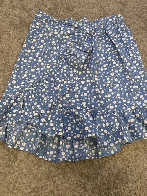 Två blommiga kjolar i blått och rött - Säljer två söta kjolar med blommigt mönster, en i blått med volang och knyt framtill och en i roströd med vita blommor och resår i midjan. Perfekta för vår och sommar, båda i lätt och luftigt material. Storlek xxs/xs, något däremellan.