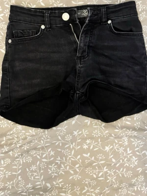 Svarta shorts med dragkedja - Snygga svarta shorts i denim med klassisk femficksdesign och dragkedja framtill. Shortsen har en knapp i midjan och raka ben. Perfekta för sommaren och passar till det mesta i garderoben.